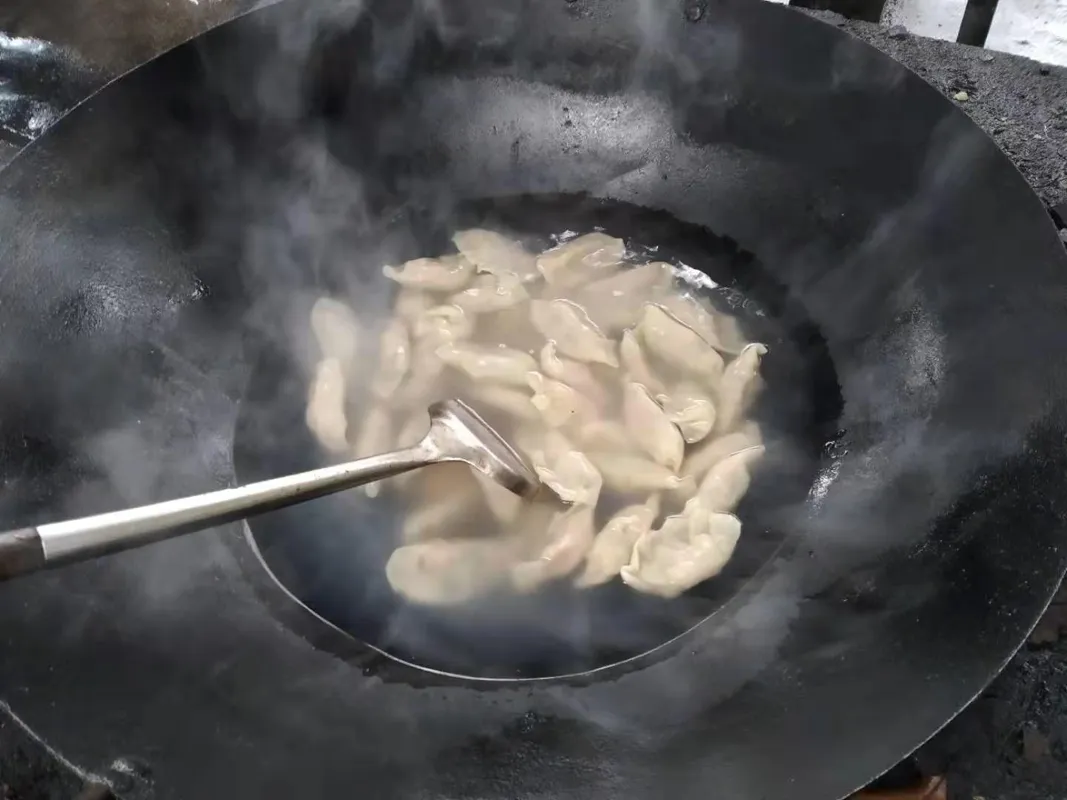 Dumplings cooking in a dark wok on an outdoor stove