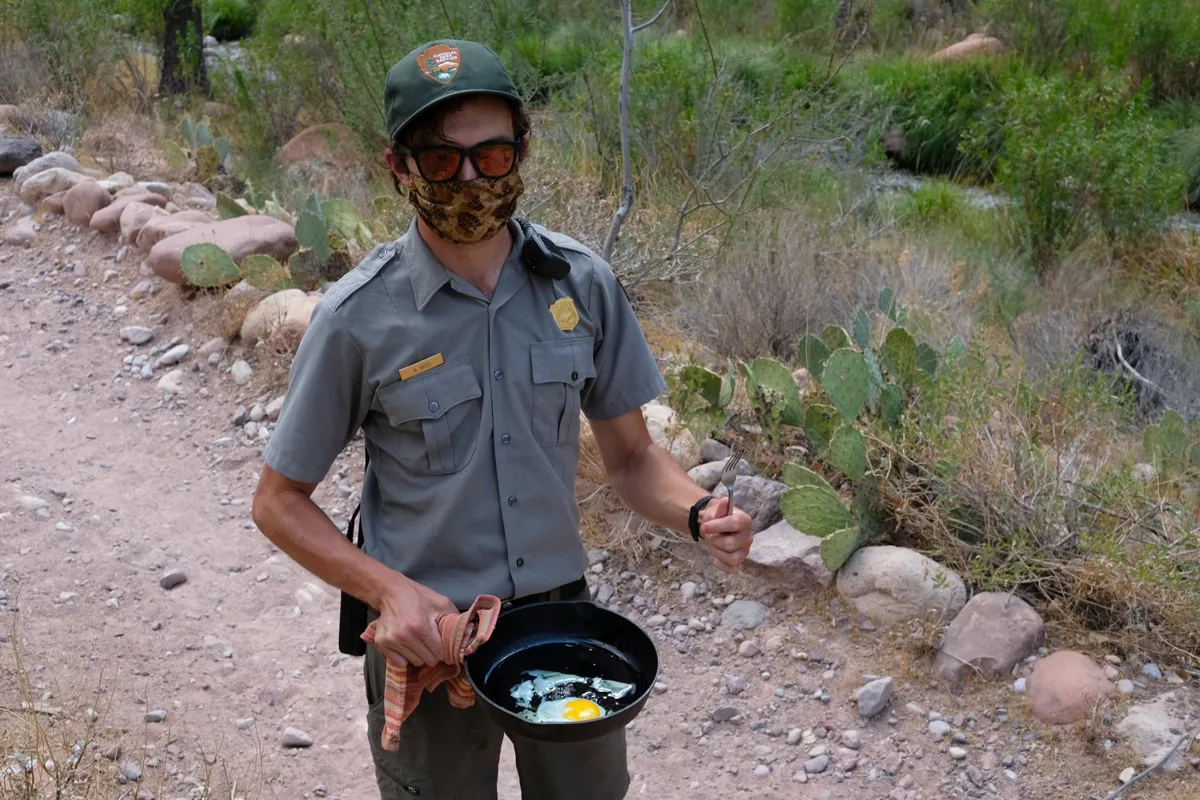Park ranger outdoors holding a small skillet with a fried egg